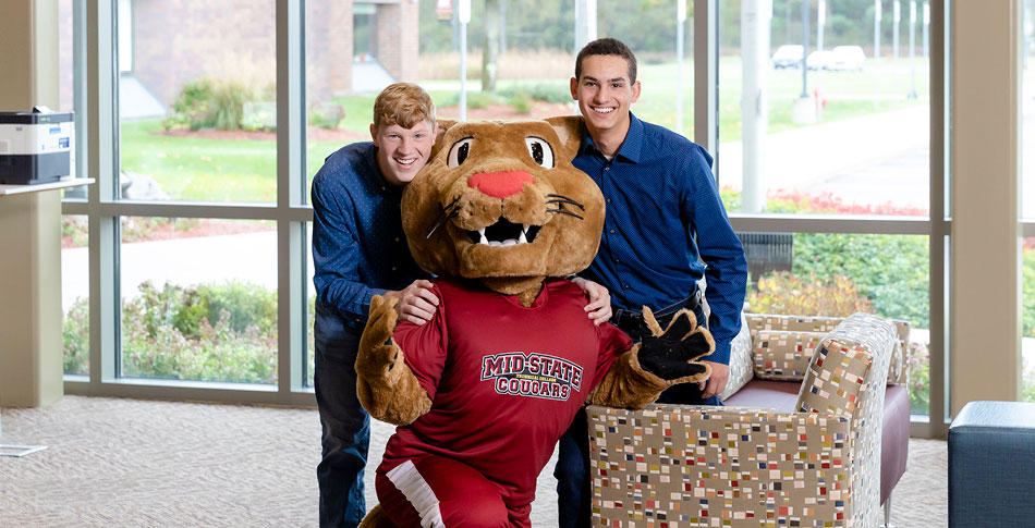 Grit, Mid-State's Cougar mascot, kneeling next to two students.