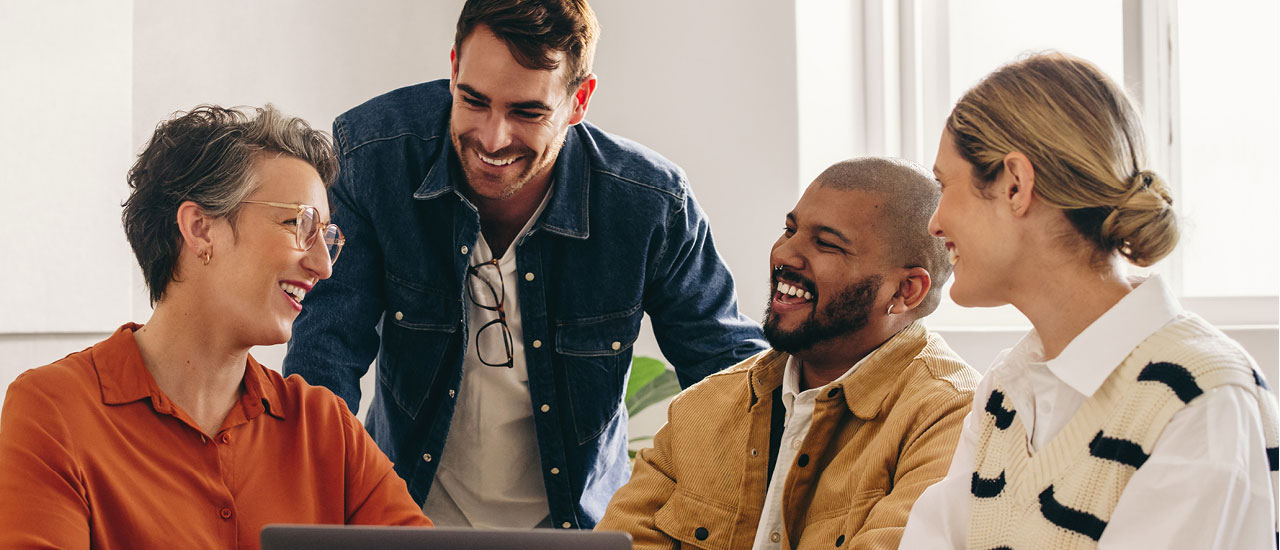 4 people sitting around a laptop smiling at each other