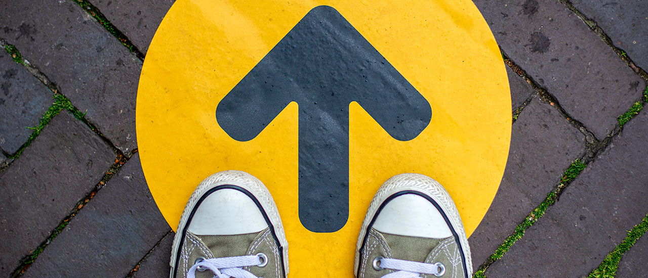 Close up of a person's shoes standing on a yellow circle with a black arrow pointing forward
