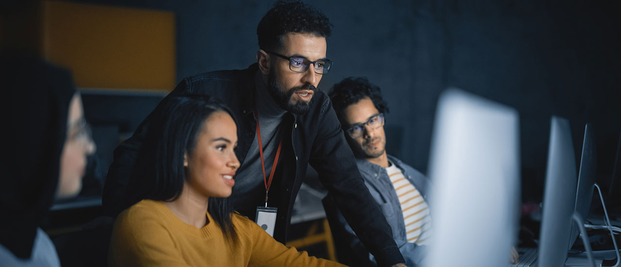 Four people looking at a desktop computer. One person is standing.