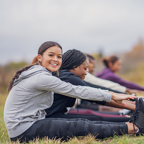 Teenagers stretching while sitting on the ground outside.