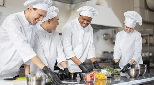 4 people in chef garb preparing fruits and vegetables in a kitchen