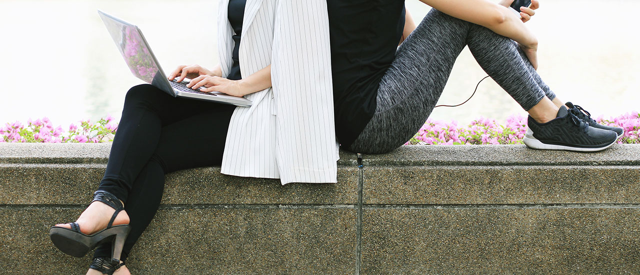 Two people sitting on a bench. One is business clothes and the other in workout clothes.