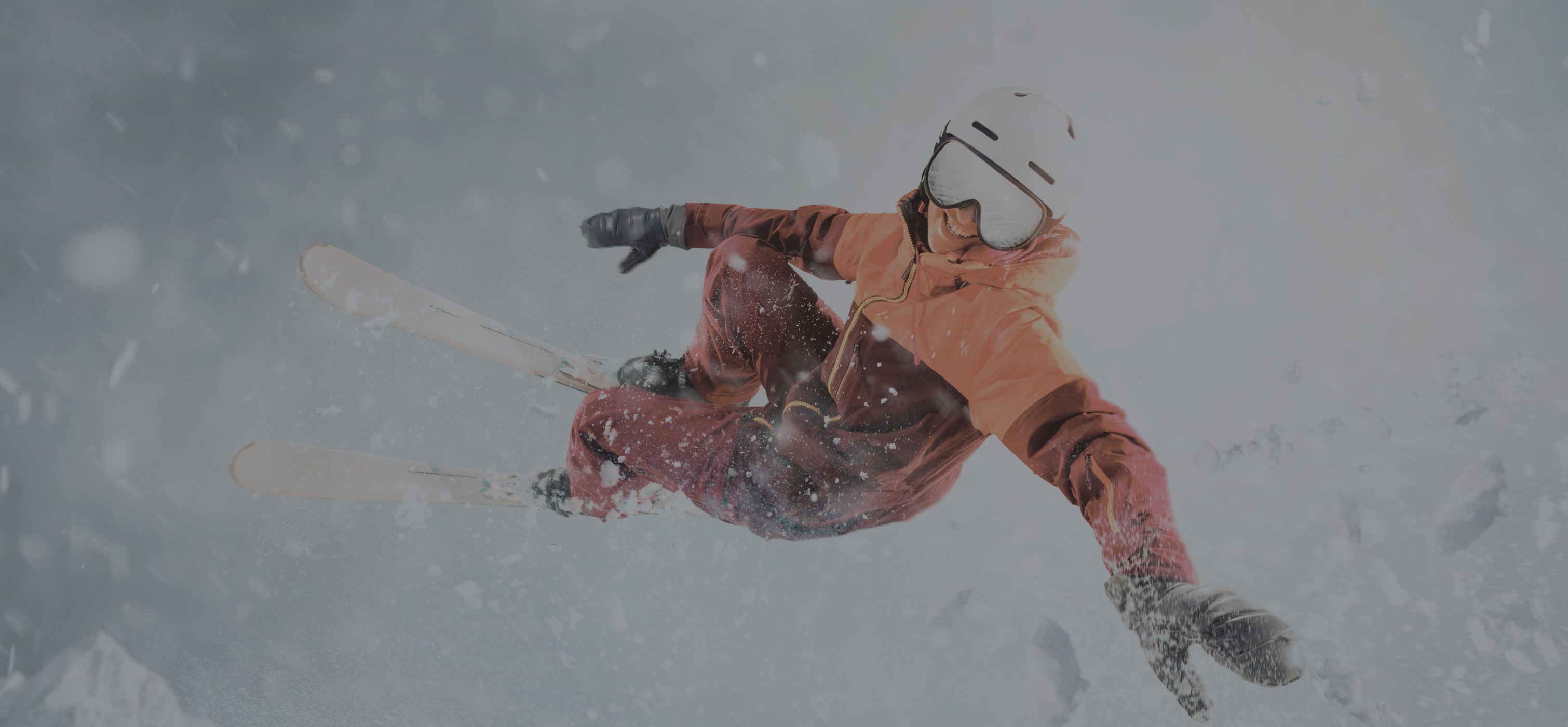 Person in the air with snow all around them wearing skis and winter attire