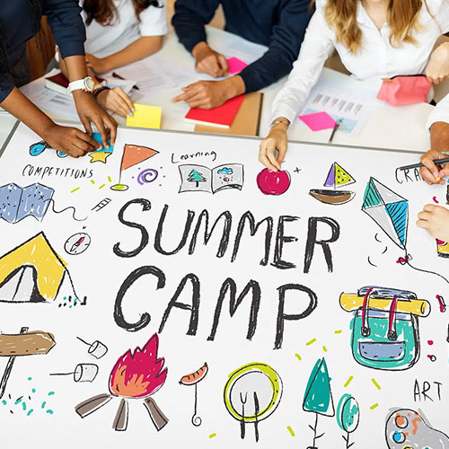 Summer camp and related images drawn on a posterboard with people sitting around it.