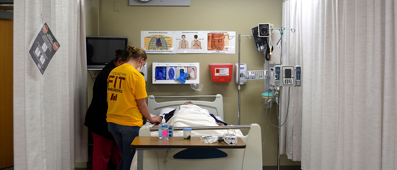 HealthQuest attendee practices taking blood pressure on a manakin alongside a Mid-State Nursing instructor.