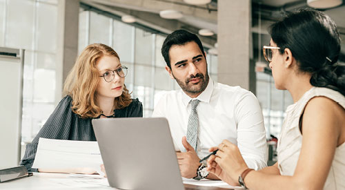 3 people sitting around a laptop having a conversation