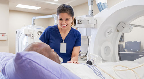 Person in scrubs talking to a patient about to go into an MRI machine