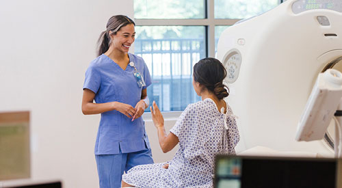 Person in scrubs talking to a patient sitting down next to an MRI machine