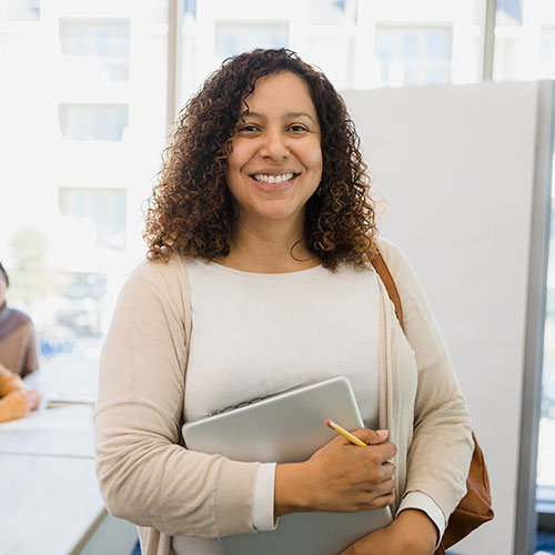 Person smiling at the camera holding a laptop and pencil.