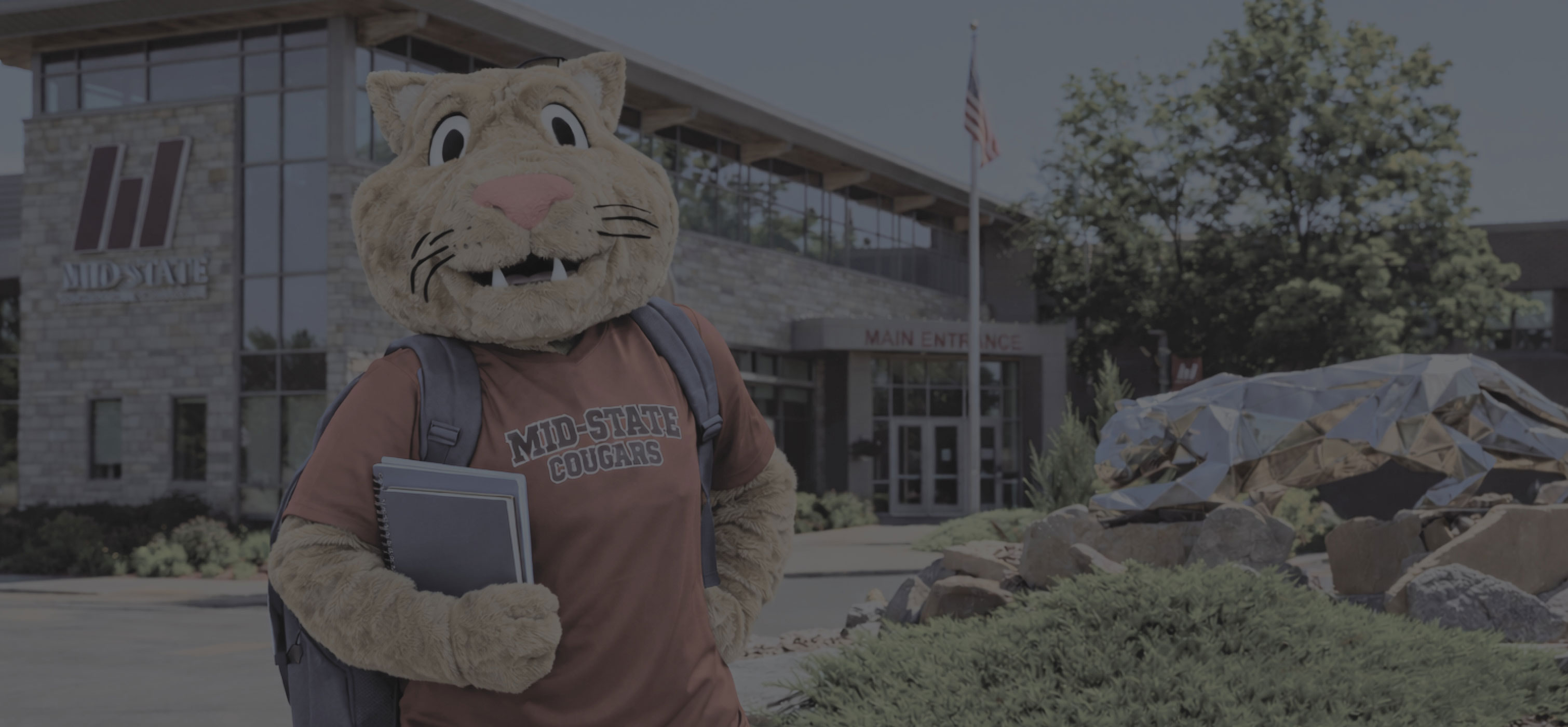 Mid-State Mascot Grit standing in front of the Wisconsin Rapids Campus building