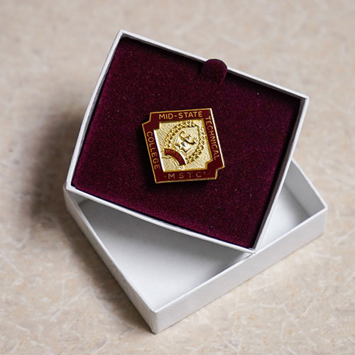 Mid-State’s Nursing pin, which depicts a lamp and a book.