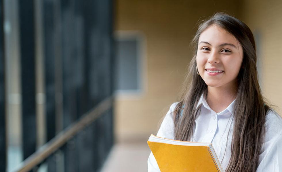 A student smiling at the camera and holding a notebook.