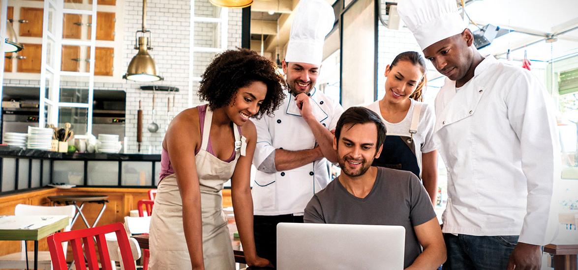 Culinary workers in uniform gather around a laptop.