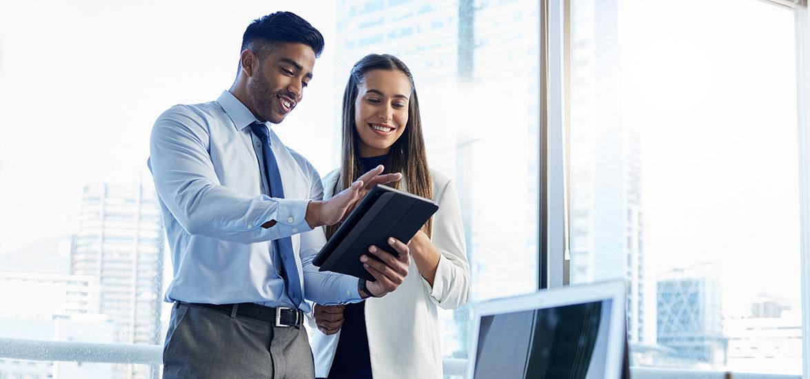 Two people in business professional attire look at an electronic device.