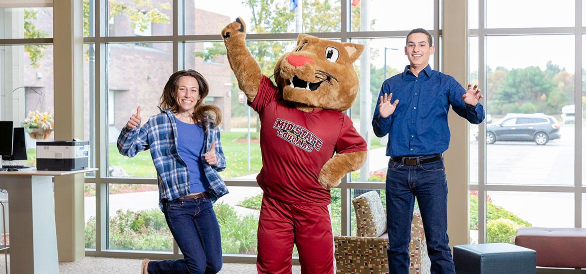Two teenage students jumping alongside Mid-State Technical College cougar mascot, Grit.