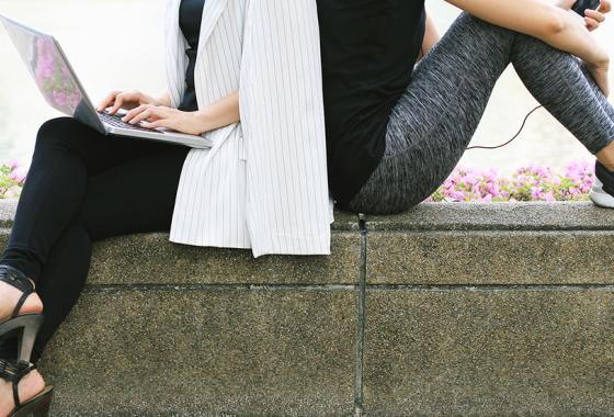 Two people sitting on a bench outside. One is in business clothes and one is in exercise clothes.